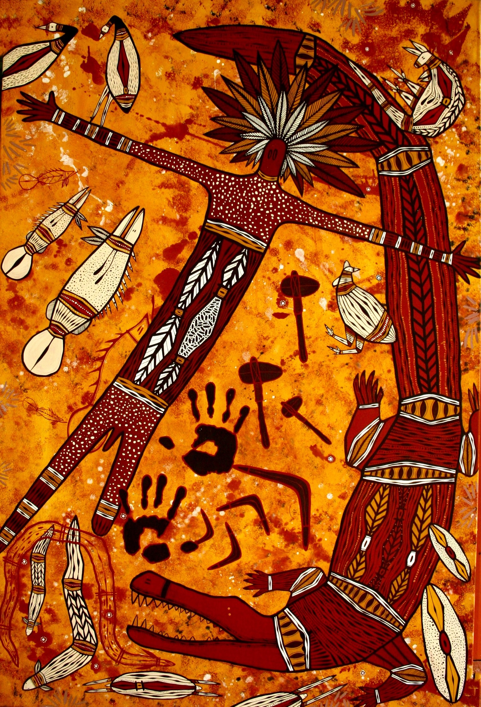 indigenous painting depicting a male figure with headdress and crocodile. Colours are red, black, orange and white. Around the male figure and crocodile the image depicts smaller Australian animals, axes, hand prints and boomerang.